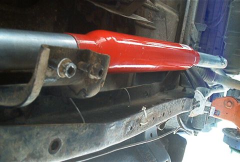 1986 Ford Bronco - Undercarriage view of a red shock absorber mounted to a vehicle frame.