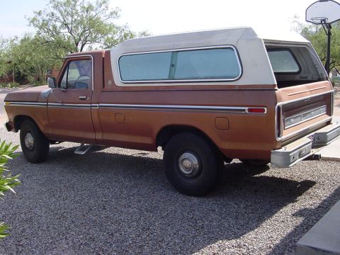 1977 Ford F-250 - This pickup truck features a two-tone paint scheme and a white camper shell, parked on a gravel surface.