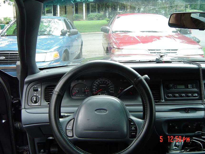 Interior view of a blue car, showing dashboard and steering wheel. Two other cars, a red and a blue sedan, are visible through the windshield