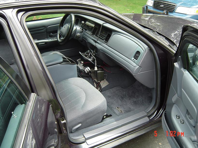 Dark purple sedan interior, gray cloth seats, dashboard with radio and vents. Another blue car is visible outside
