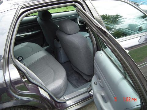 1999 Ford Crown Victoria - The interior of a dark sedan is visible with both rear doors and the driver's side front door open, revealing the back seats and dashboard.