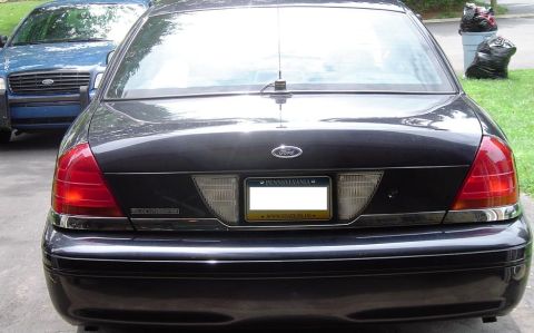 1999 Ford Crown Victoria - Two sedans are parked outdoors, one dark and one blue, with trash bins in the background.