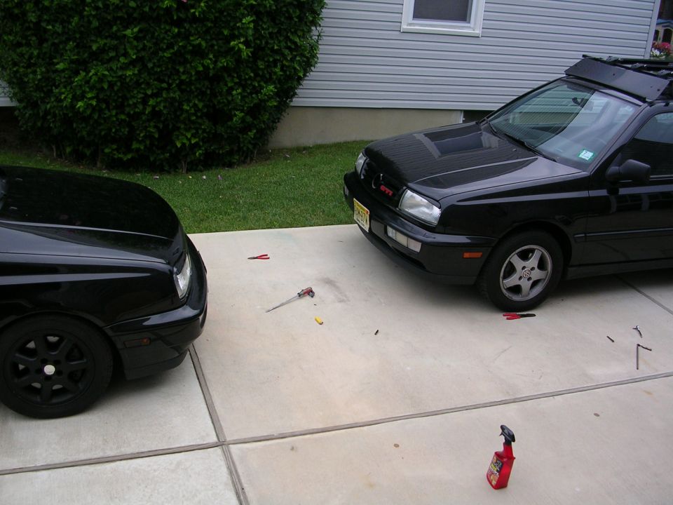Two black VW Mk3 GTI hatchbacks facing each other on a driveway with tools scattered on the concrete