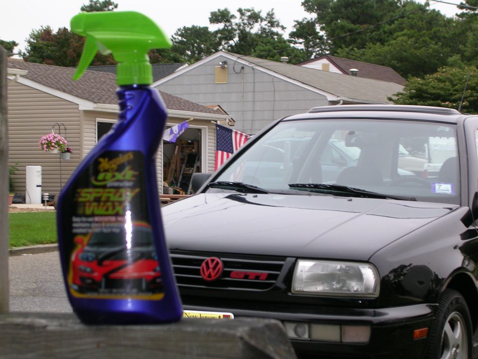 Meguiar's spray wax bottle in foreground with black VW GTI and house behind