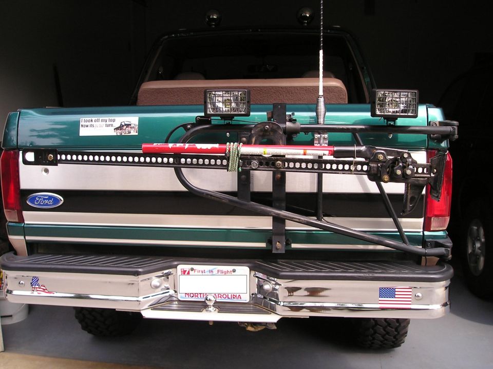 Rear of teal Ford SUV with swing-out tire carrier rack, off-road lights and jack