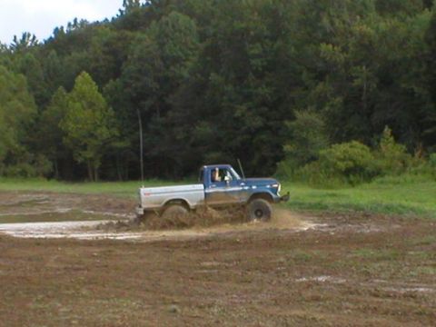 1979 Ford F-150 - A pickup truck navigates a muddy off-road course, kicking up dirt and water.