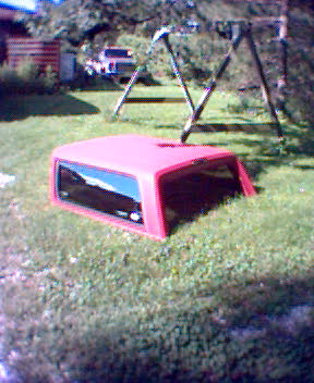 1994 Ford Bronco - A red truck cap is partially buried in the grass next to a swing set.