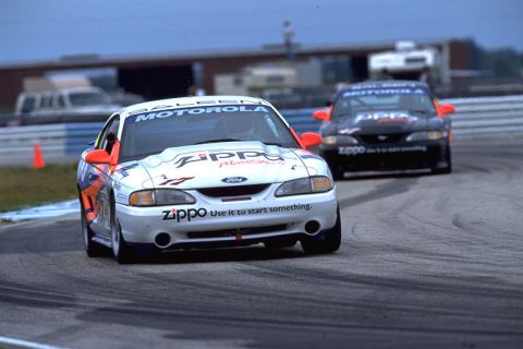1995 Ford Mustang - Two Ford Mustangs, one white with Zippo sponsorship and another black, compete on a race track.