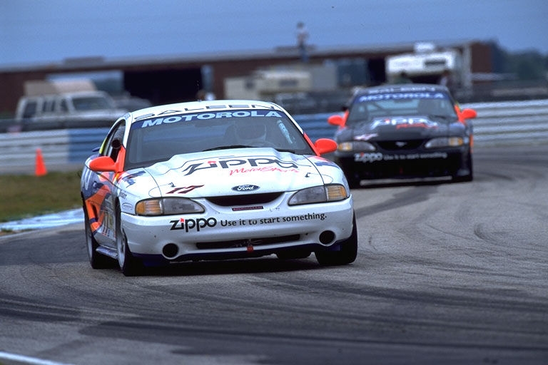 White 1995 Ford Mustang race car with orange accents and Zippo livery on track