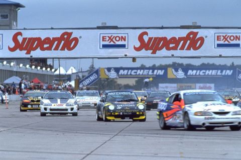 1995 Ford Mustang - Multiple race cars compete on a track under a Superflo and Exxon banner.