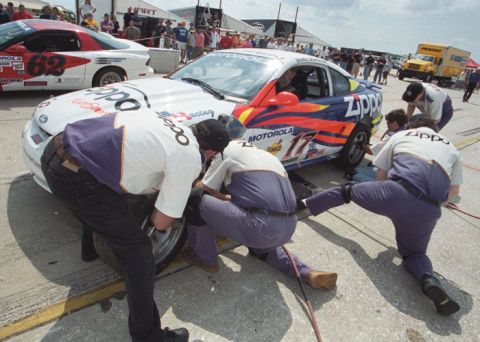 1995 Ford Mustang - Pit crew works on a race car during a stop, with another car visible in the background.