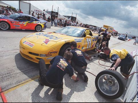 1995 Ford Mustang - Pit crew services a yellow Chevrolet Corvette C5 race car during a competition.