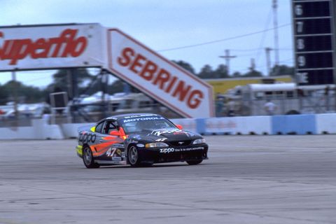 1995 Ford Mustang - Race car identified as a 1995 Ford Mustang speeds around a track with sponsor decals.