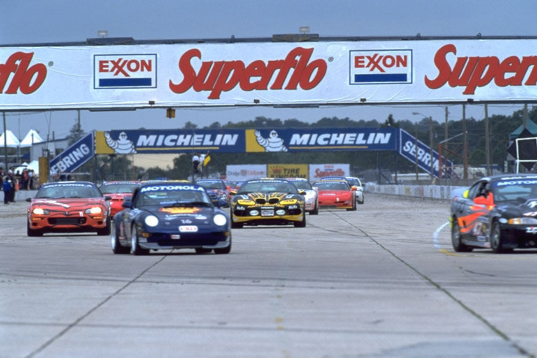 Several race cars on a track, with a large Superflo and Exxon banner overhead. Some cars have Motorola sponsorship