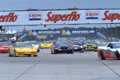 1995 Ford Mustang - Multiple race cars, including a black 1995 Ford Mustang, compete on a track under a Superflo banner.