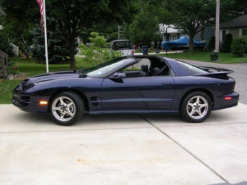 2000 Pontiac Trans Am - A dark blue Pontiac Firebird is parked on a concrete driveway in front of a suburban house.