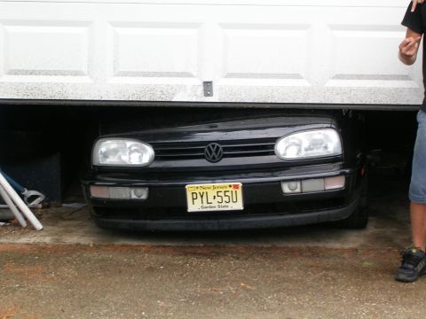1990 Jeep YJ - A black Volkswagen Golf is barely fitting under a closed garage door.