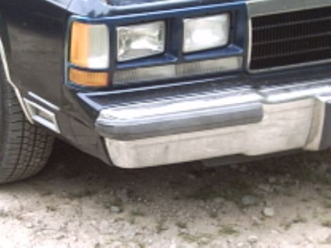 1990 Ford Crown Victoria LTD - The front corner of a car is visible, with a prominent chrome bumper and rectangular headlights.