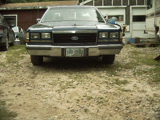 Dark blue Ford Crown Victoria, front view, parked on gravel lot