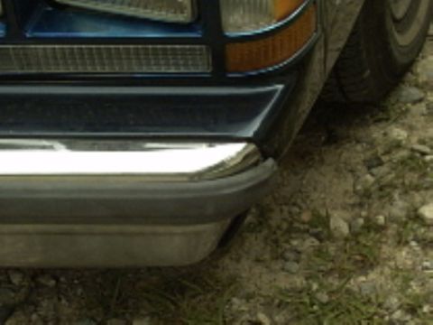 1990 Ford Crown Victoria LTD - Close-up of the front corner of a dark blue car, showing the bumper and headlight assembly.