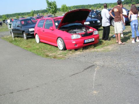 1990 Jeep YJ - A red hatchback with its hood open is parked on grass next to other vehicles at an outdoor event.