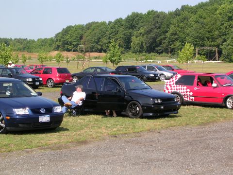 1990 Jeep YJ - Cars gathered on a grassy field under a clear sky, with a line of trees forming the backdrop.