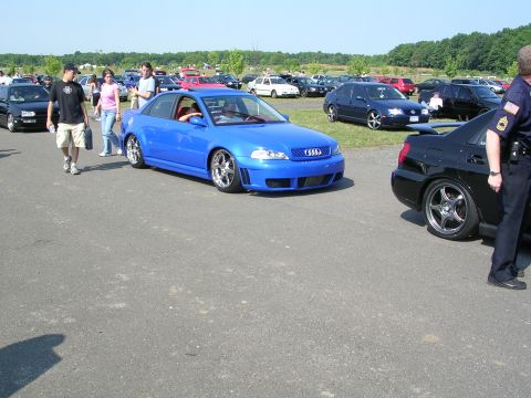 1990 Jeep YJ - A bright blue Audi sedan is the focus of this outdoor car show scene, with other vehicles and attendees around.