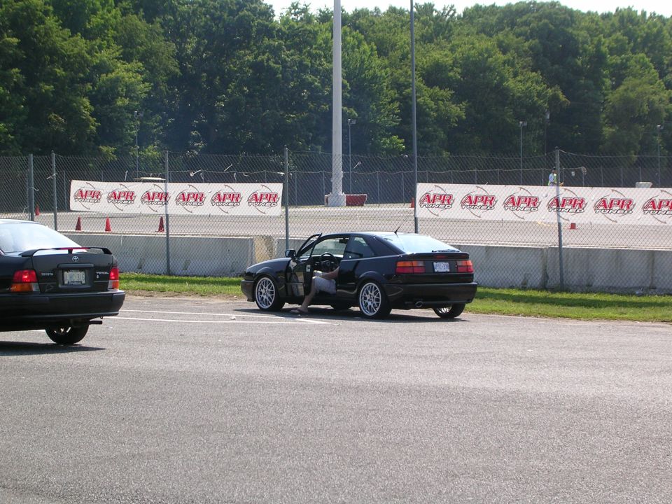 Black Volkswagen Corrado with driver's door open, parked on asphalt. Another black car is visible to the left