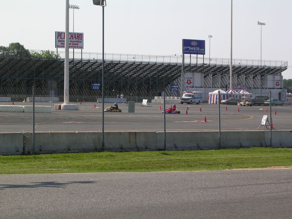 Go-karts racing on a track with grandstands and tents in the background