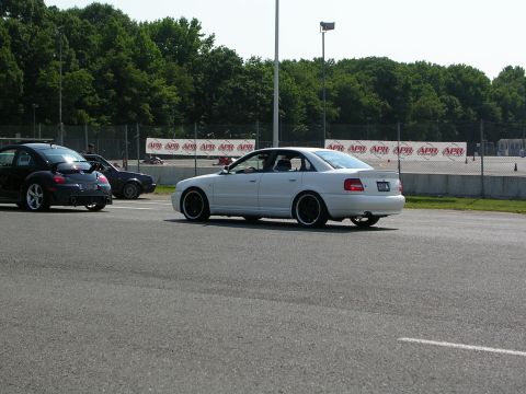 1990 Jeep YJ - A white sedan with black wheels drives on a race track alongside other vehicles.