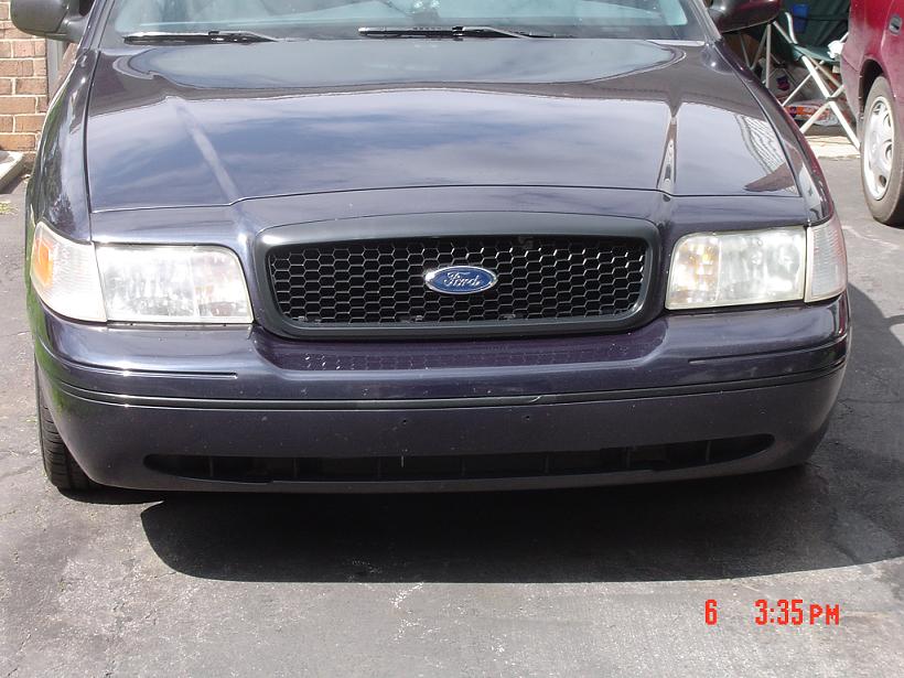 Front end of a dark Ford Crown Victoria with Ford-badged mesh grille and aftermarket lower bumper cover