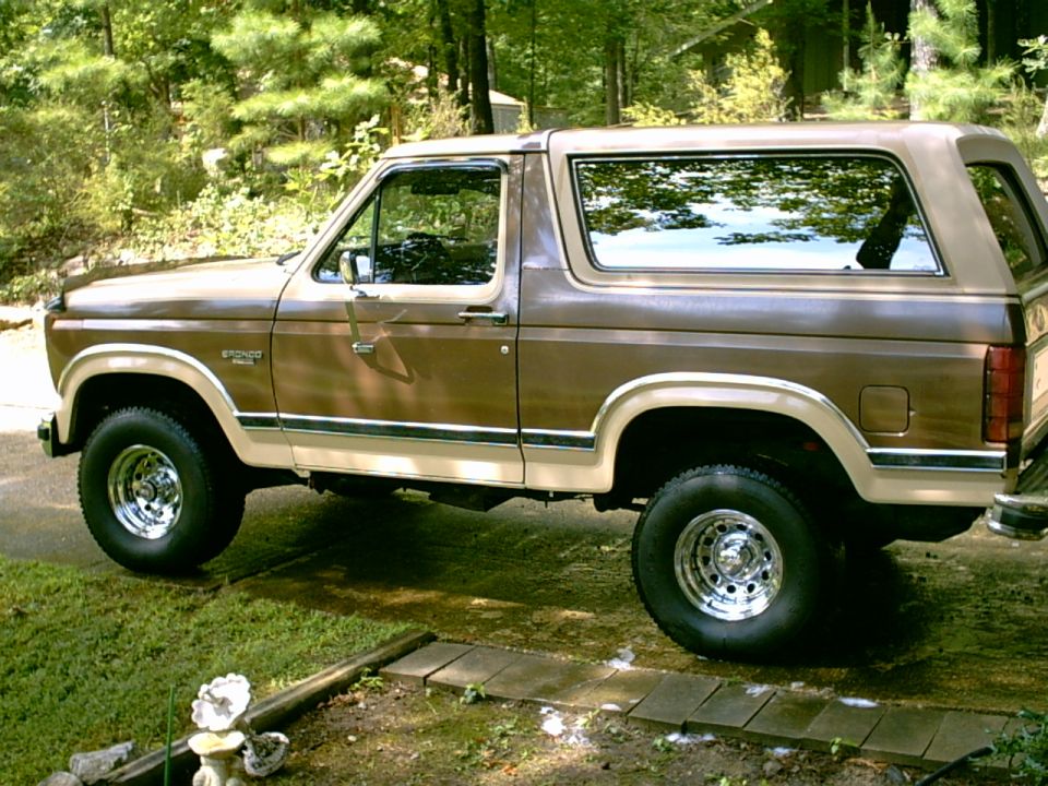 Brown 1980s Ford Bronco SUV parked on a grassy area with trees in the background
