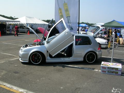 1990 Jeep YJ - A silver hatchback is displayed with its hood and doors open, custom modifications at an outdoor event.