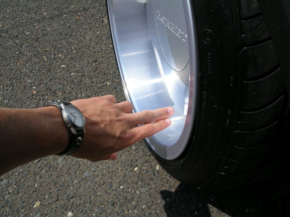 Person's hand with a watch pointing at a polished alloy wheel and tire