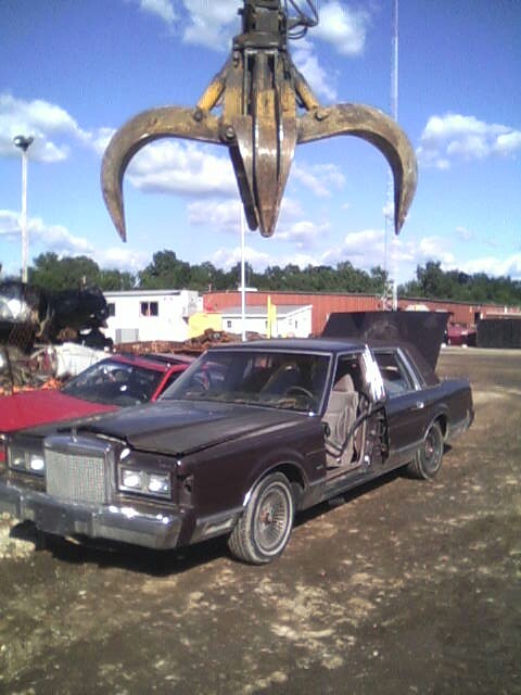 1986 Lincoln Town Car - A brown Lincoln Town Car sits in a junkyard with its doors and hood open, awaiting a car claw.