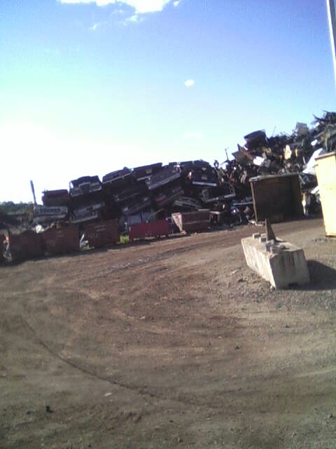 1986 Lincoln Town Car - A large pile of wrecked vehicles sits in a junkyard under a clear blue sky.