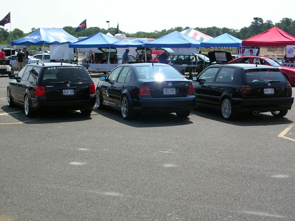 Three black Volkswagens parked outside with tents in the background