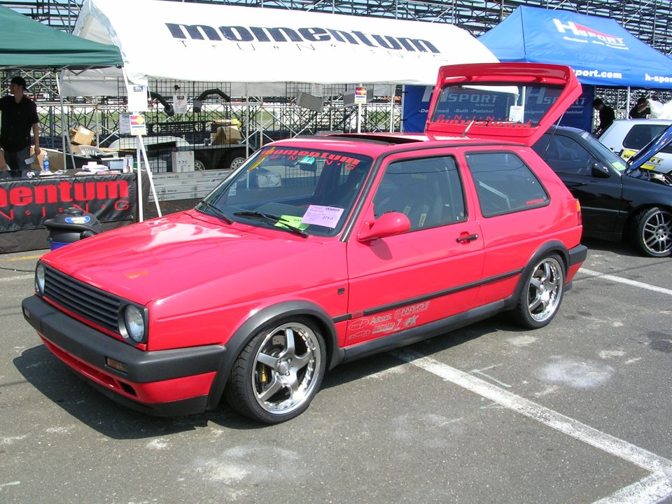 Red 1990s Volkswagen Golf GTI with aftermarket spoiler and wheels parked at an event