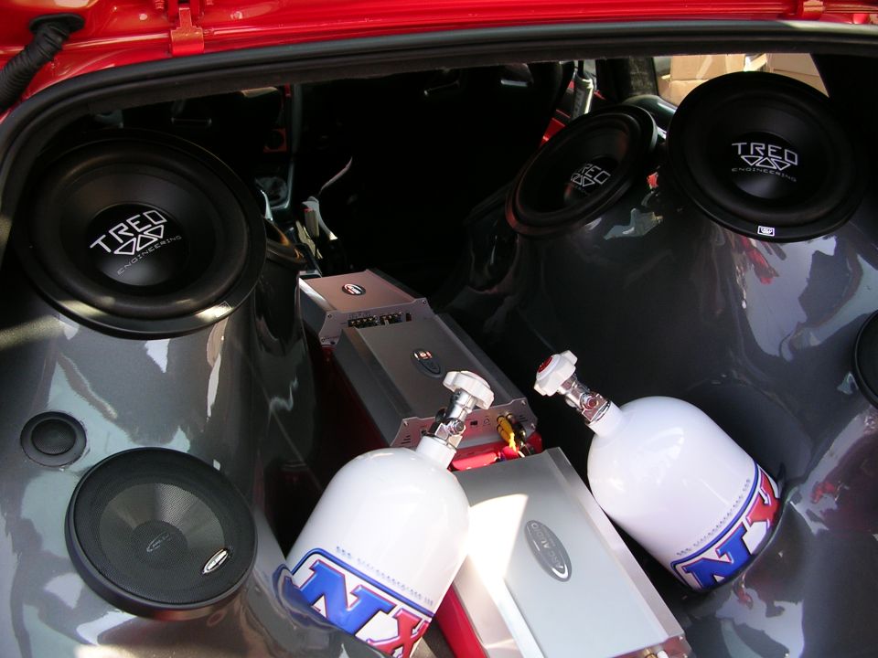 Car trunk filled with multiple subwoofers, amplifiers, and two NX nitrous oxide bottles