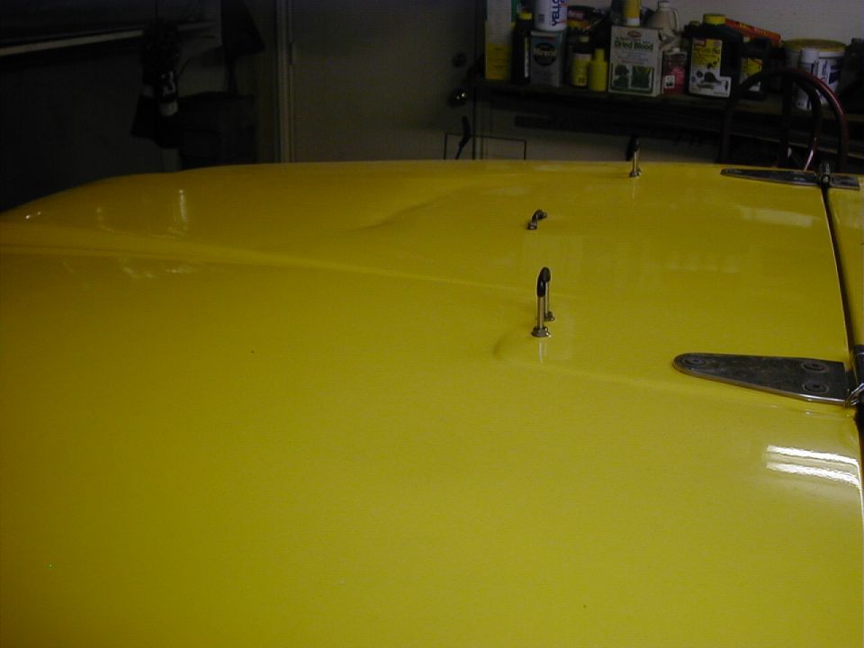 Yellow vehicle hood showing paint crease damage, in a garage setting
