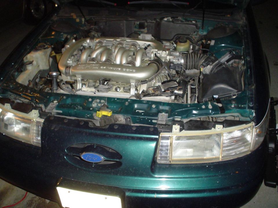 Open engine bay of a green Ford sedan with DOHC V6 engine and the blue Ford oval on the front nose