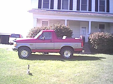 1994 Ford Bronco - A two-tone red and grey pickup truck is parked in front of a house with another vehicle visible in the background.