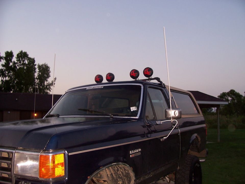 Dark blue Ford Bronco with four roof-mounted off-road lights and whip antennas at dusk