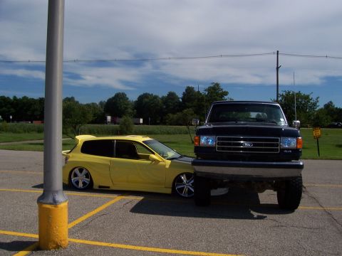 1989 Ford Bronco - A black 1989 Ford F-Series truck is parked in front of a yellow Honda Civic.