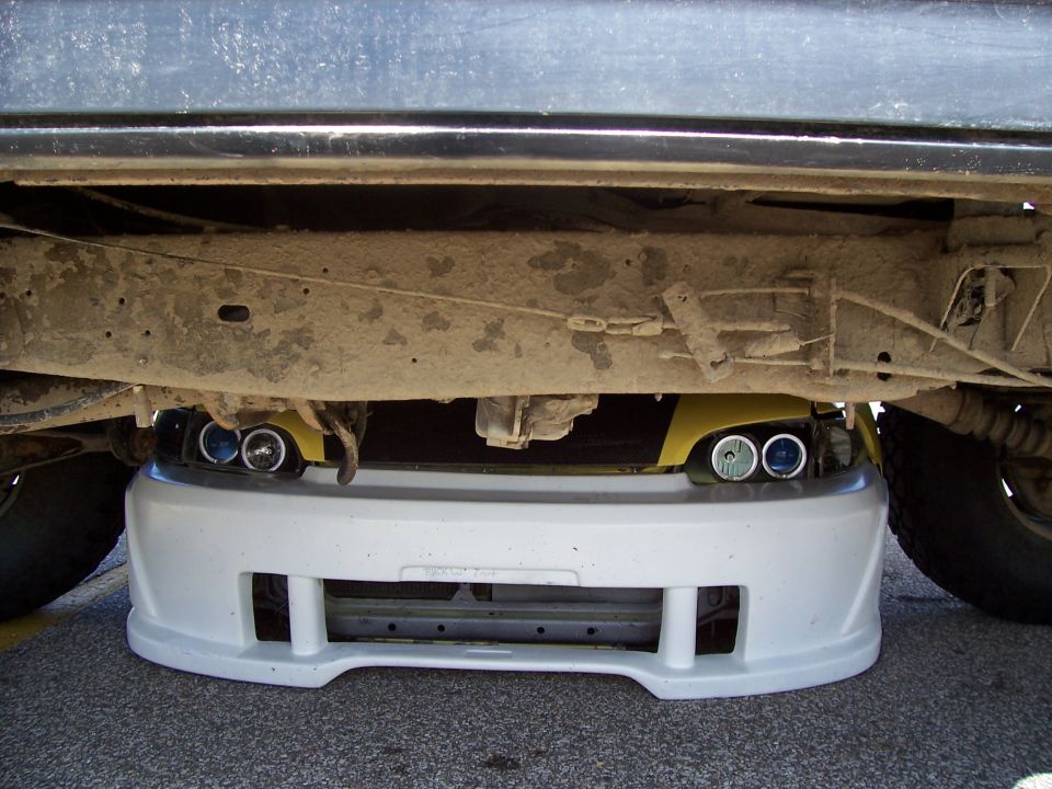 Yellow car's front bumper and headlights are visible underneath a larger vehicle