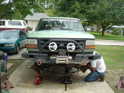 1993 Ford Bronco - A person works on the front suspension of a 1993 Ford Bronco, which is raised on jacks.