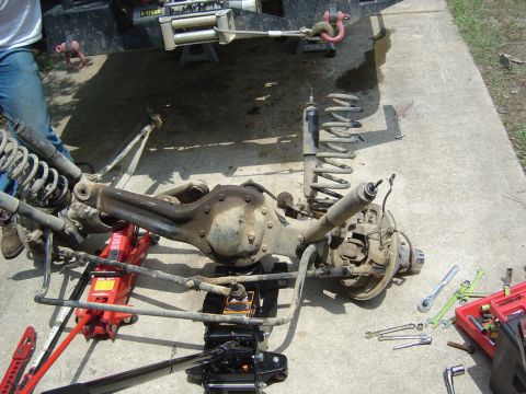 1993 Ford Bronco - A disassembled rear axle assembly with shocks and springs is supported by jacks, with various tools nearby.
