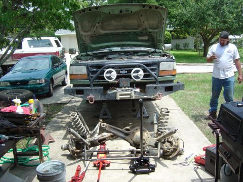 1993 Ford Bronco - A green Ford Bronco is undergoing maintenance with its front axle removed, while a man stands nearby.