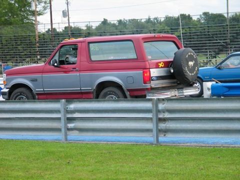 1995 Ford Bronco - Side view of a red and gray 1995 Ford Bronco parked next to a blue car on a track.