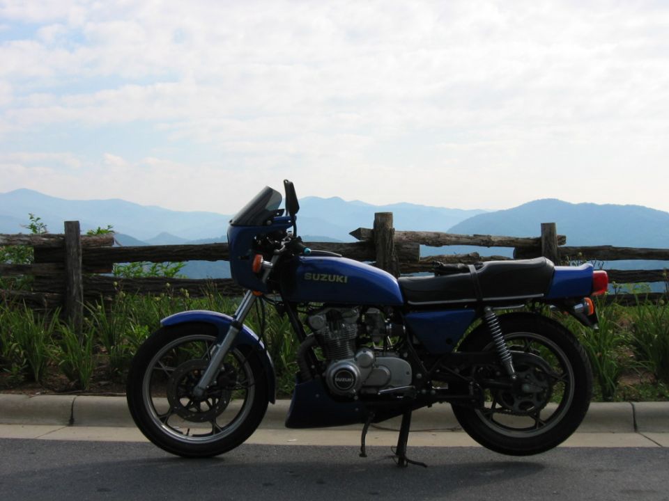 Blue Suzuki motorcycle parked on roadside with mountains in background